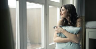 black haired woman hugging gray pillow near glass panel window